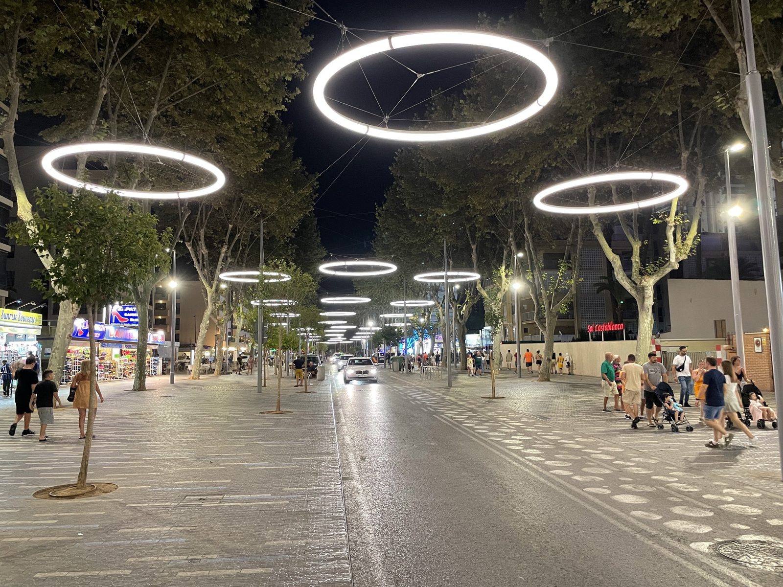 A Benidorm street at night with large rings of light above the road