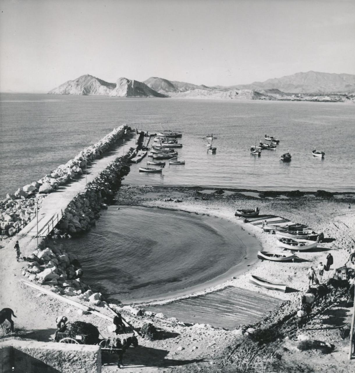 um 1930: Die Hafenmole mit den Fischerbooten. Dahinter liegt der Strand von Poniente – leer.